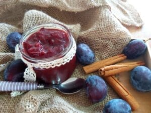 A jar filled with homemade plum jam next to plums and cinnamon.