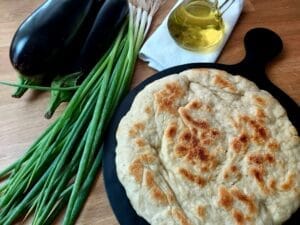 Baked round bread on a black platter next to a bunch of spring onions.