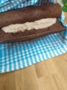 The base for a Swiss roll with filling is rolled up using a kitchen towel.