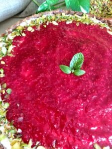 Pistachio Raspberry Tart garnished with chopped pistachios and mint leaves.
