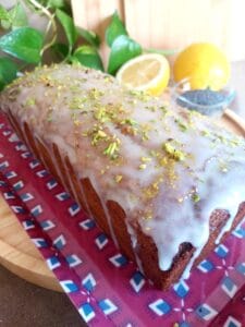 Glazed loaf cake topped with chopped pistachios on a decorative platter.