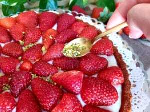 A hand spreading chopped pistachios on top of a strawberry cake.