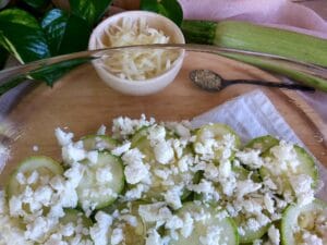 Layered zucchini slices in a baking dish and covered with crumbled feta cheese.