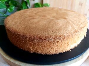Baked and cooled Italian Sponge Cake on a black platter ready for garnish. 