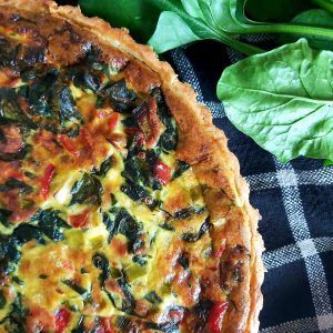 Baked spinach quiche on a dark table cloth.