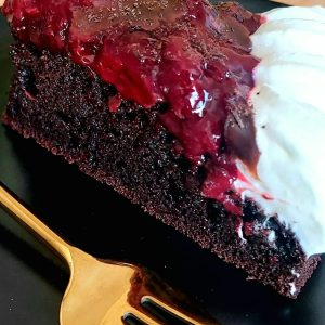 Slice of a chocolate cake filled with cherries and topped with whipped cream